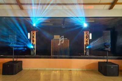 Scène avec équipement de sonorisation, éclairage coloré et projecteurs, dans une salle aux murs clairs et plafond en bois.