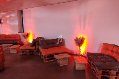 Canapés en palettes avec coussins orange et tables basses en bois, éclairés par une lumière chaude dans une salle moderne.