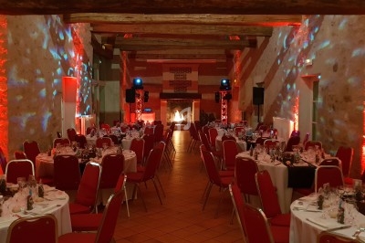 Salle de réception décorée avec des lumières rouges, tables dressées et chaises rouges alignées.