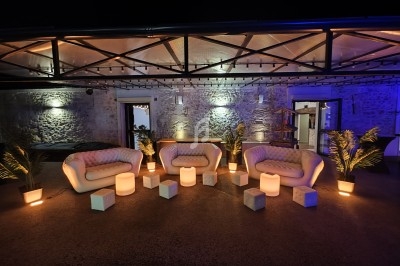 Espace extérieur aménagé avec des fauteuils, cubes lumineux et plantes, éclairé par une lumière tamisée en soirée.