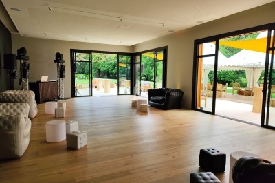 Salle lumineuse avec parquet, mobilier moderne et grandes baies vitrées donnant sur une terrasse et un jardin verdoyant.