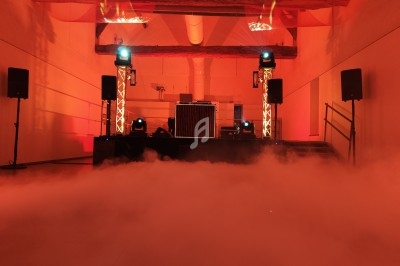 Salle de réception avec éclairage rouge, scène équipée de matériel de sonorisation et fumée au sol.