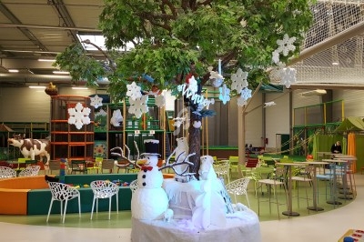 Espace de jeux intérieur avec décorations hivernales, incluant un arbre central, un bonhomme de neige et des tables colorées.