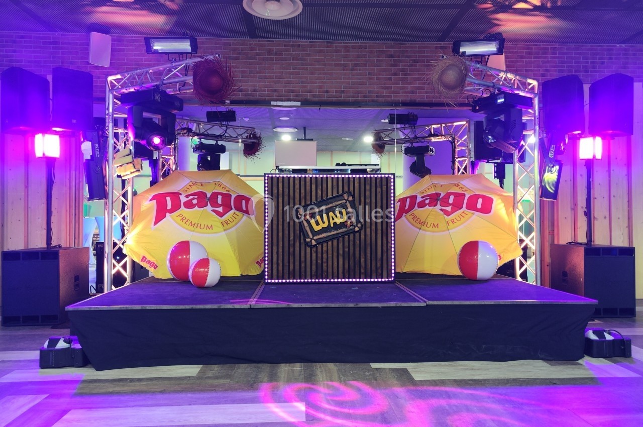 Scène décorée avec parasols jaunes, projecteurs colorés et une caisse en bois marquée ’Luau’.