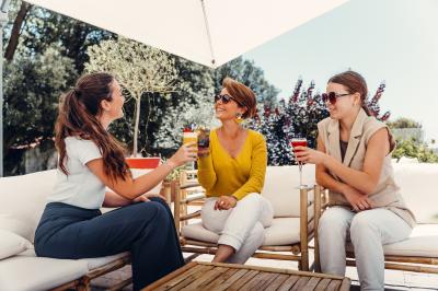 Un homme verse du vin dans une carafe en verre, en extérieur, avec des plantes floues en arrière-plan.