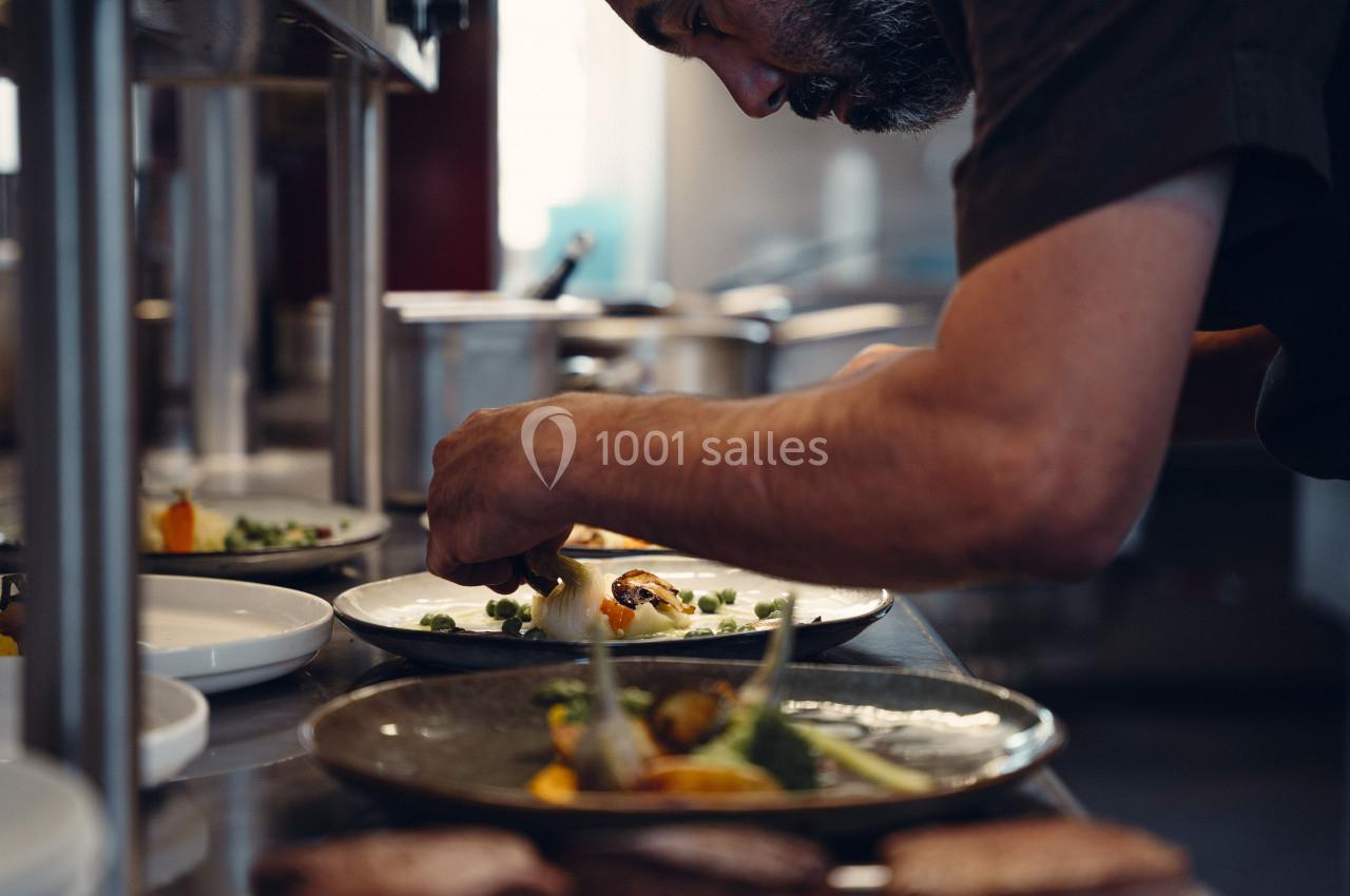 Un chef cuisine en dressant soigneusement des assiettes avec des légumes dans une cuisine professionnelle.