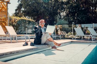 Un homme verse du vin dans une carafe en verre, en extérieur, avec des plantes floues en arrière-plan.