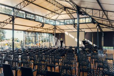 Un homme verse du vin dans une carafe en verre, en extérieur, avec des plantes floues en arrière-plan.
