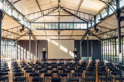 Un homme verse du vin dans une carafe en verre, en extérieur, avec des plantes floues en arrière-plan.