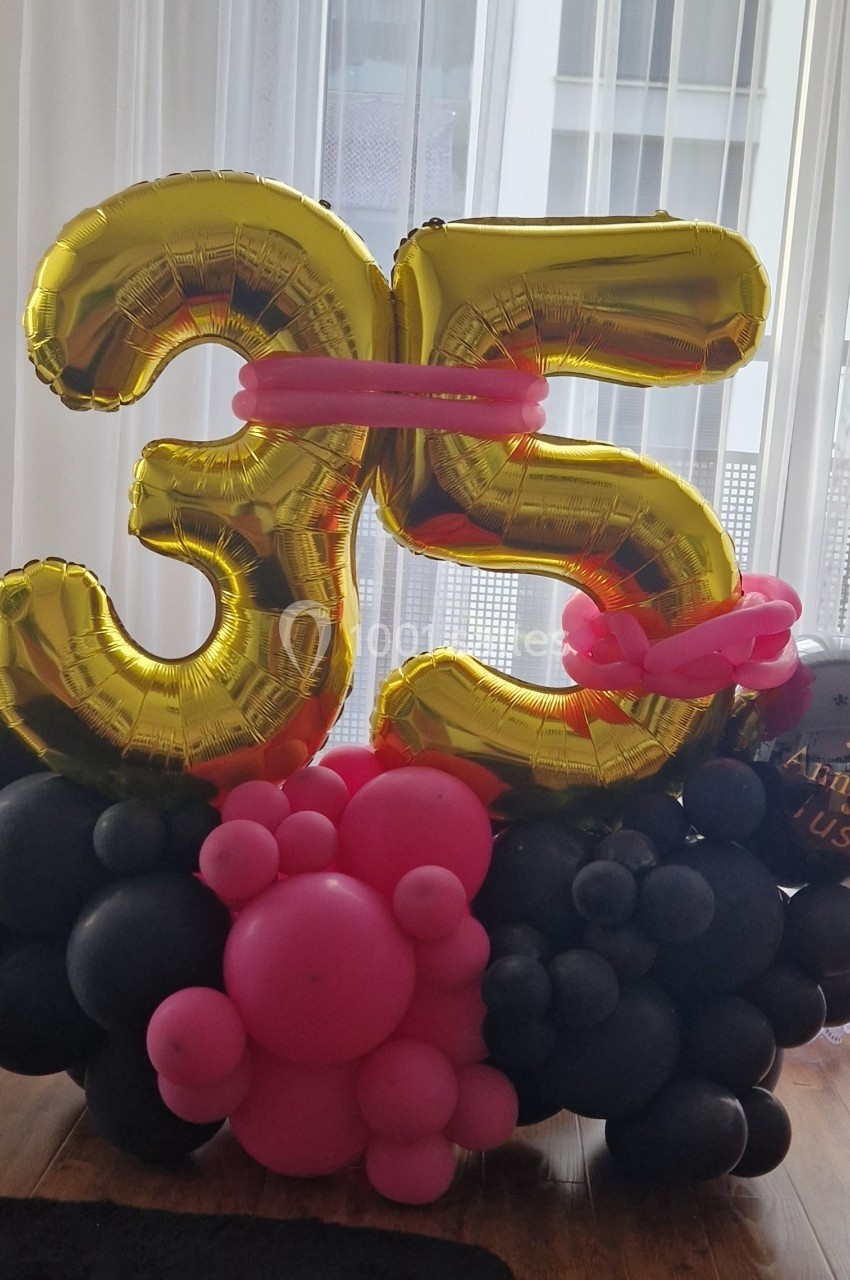 Décoration d'anniversaire avec ballons dorés formant le chiffre 35, entourés de ballons noirs et roses.