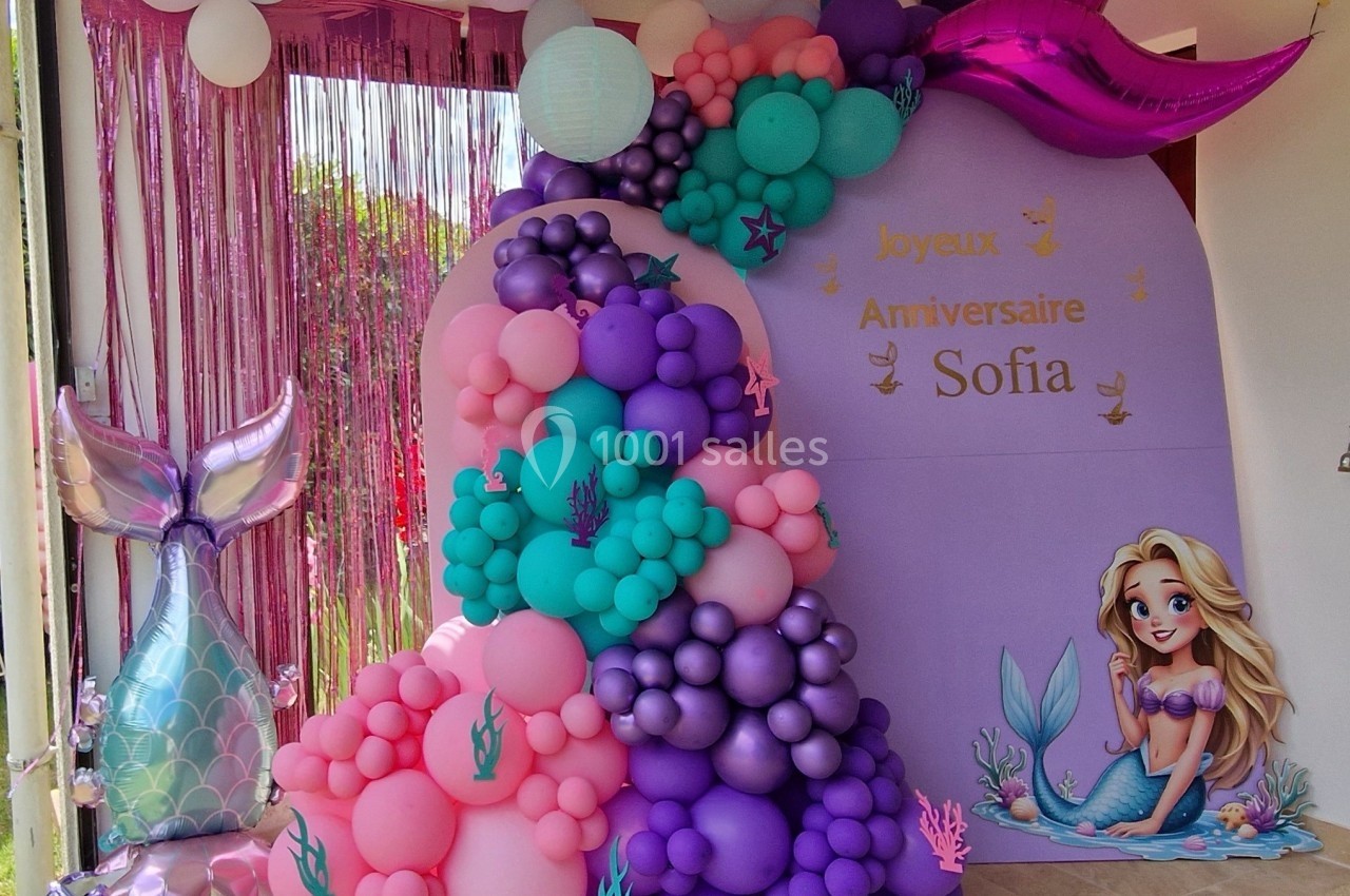 Décoration d'anniversaire sur le thème des sirènes avec ballons colorés, rideau scintillant et illustration de sirène.