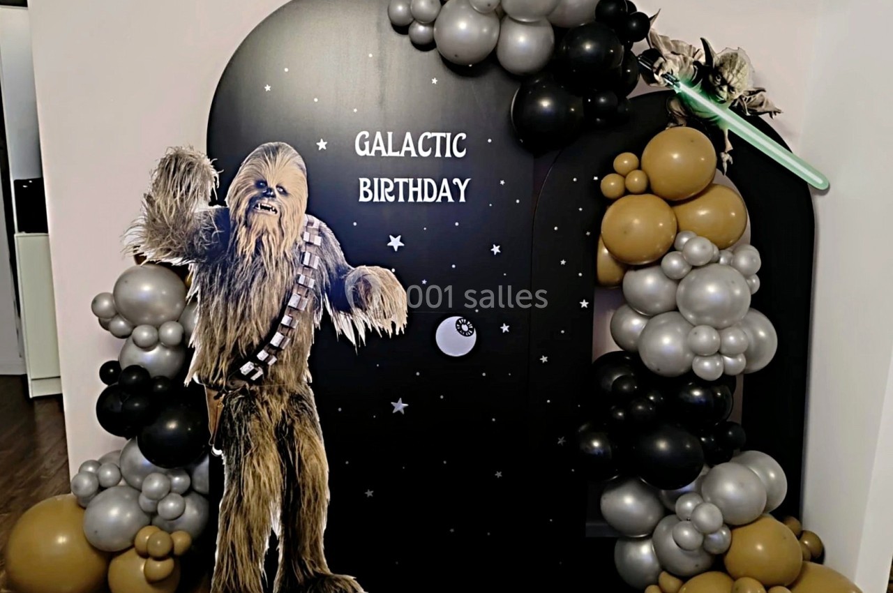Décoration d'anniversaire sur le thème galactique avec ballons argentés et dorés, et une figurine de personnage poilu.