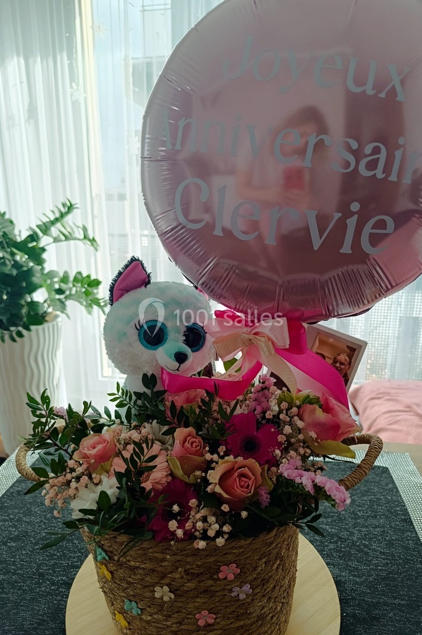 Panier en osier contenant des fleurs roses, une peluche et un ballon rose avec l'inscription ’Joyeux Anniversaire Clervie’.
