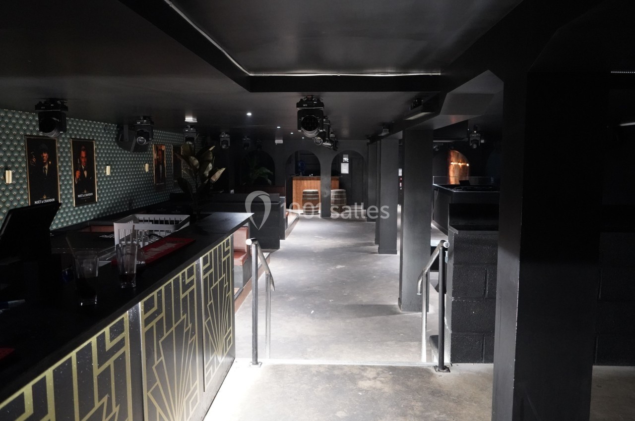 Intérieur d'un bar ou club sombre avec un comptoir, des affiches murales et un espace dégagé au sol.