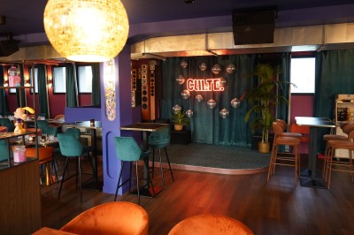 Toilettes roses décorées de mosaïques, affiches rétro sur les murs et miroir éclairé par des ampoules.