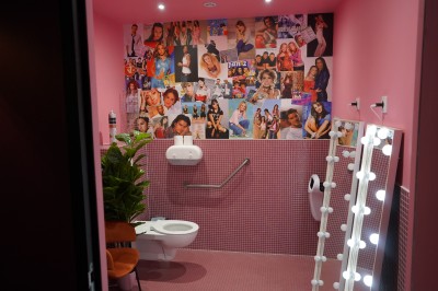 Toilettes roses décorées de mosaïques, affiches rétro sur les murs et miroir éclairé par des ampoules.