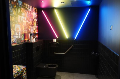 Toilettes roses décorées de mosaïques, affiches rétro sur les murs et miroir éclairé par des ampoules.