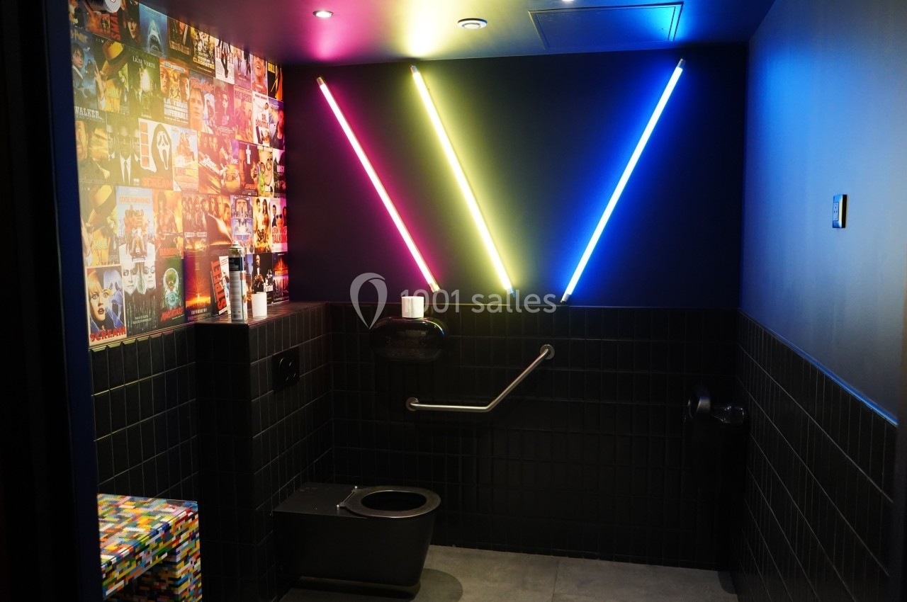 Toilettes modernes avec murs sombres, néons colorés en forme de V et décorations murales de pochettes d'albums.