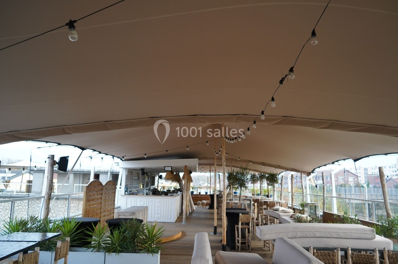 Terrasse couverte avec mobilier en bois et guirlandes lumineuses, offrant une vue sur un environnement urbain.