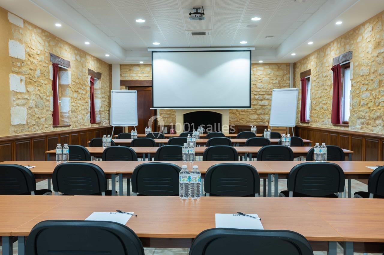 Salle de réunion équipée de tables, chaises, paperboards, bouteilles d'eau et un écran de projection.