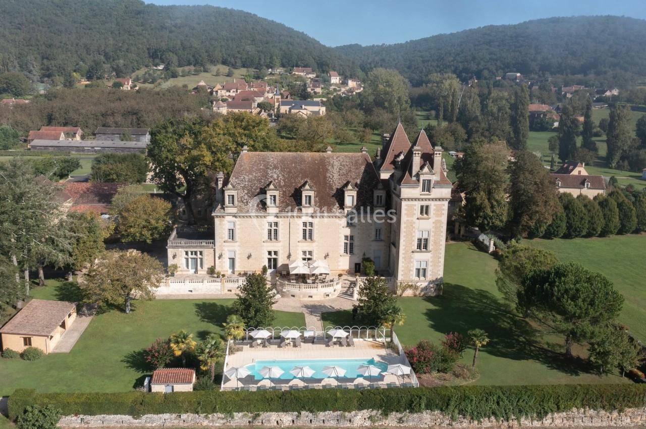 Vue aérienne d'un château entouré de jardins, avec une piscine et des collines verdoyantes en arrière-plan.
