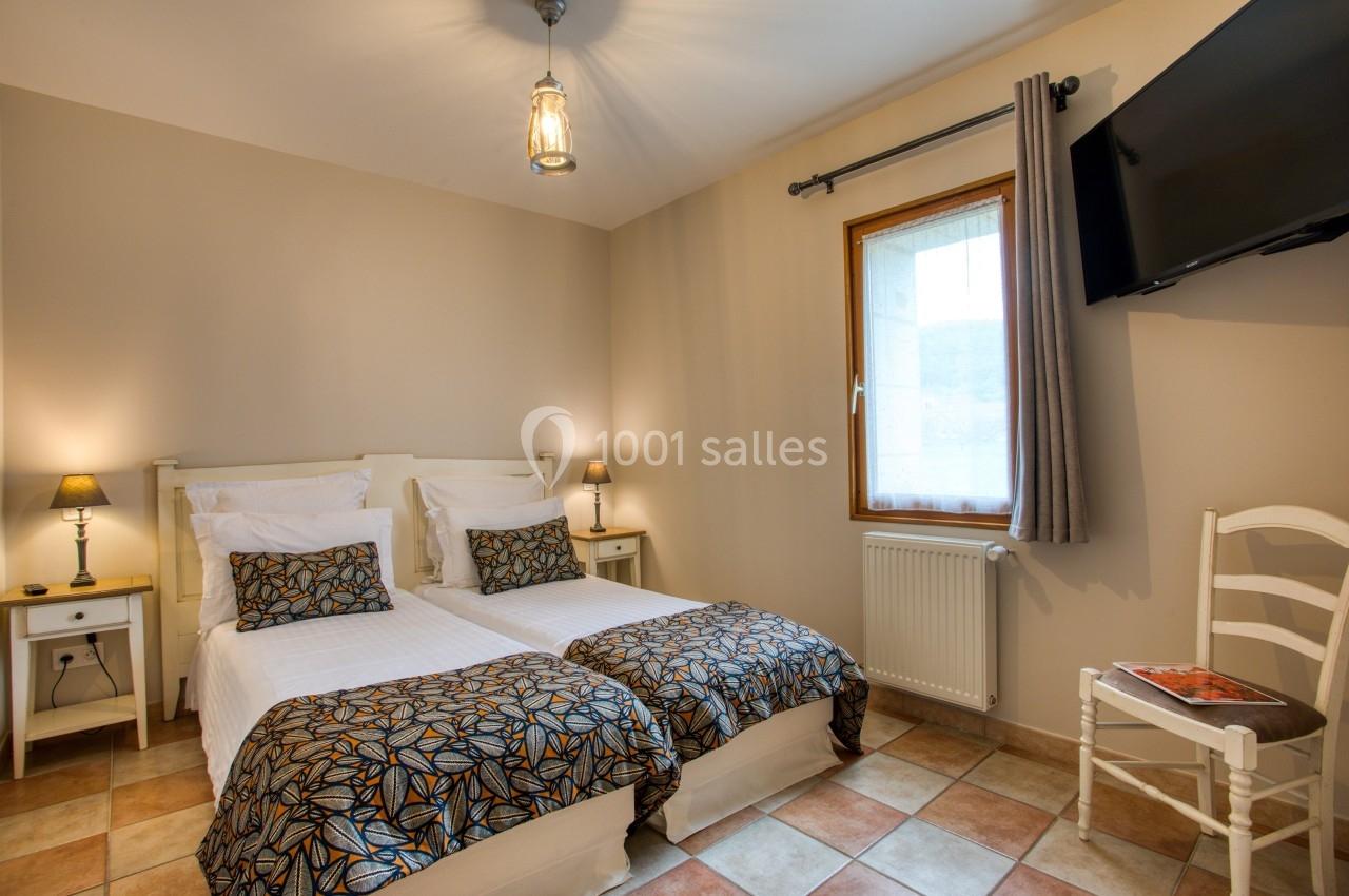 Chambre lumineuse avec deux lits simples, une fenêtre, une télévision murale et un sol en carrelage.