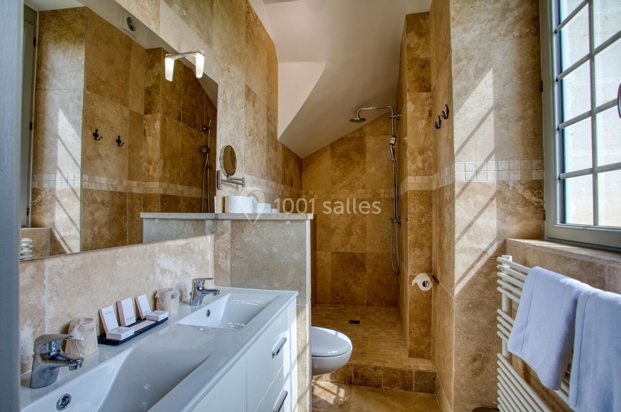 Salle de bain avec douche à l'italienne, lavabo double, miroir, murs en carrelage beige et fenêtre à droite.