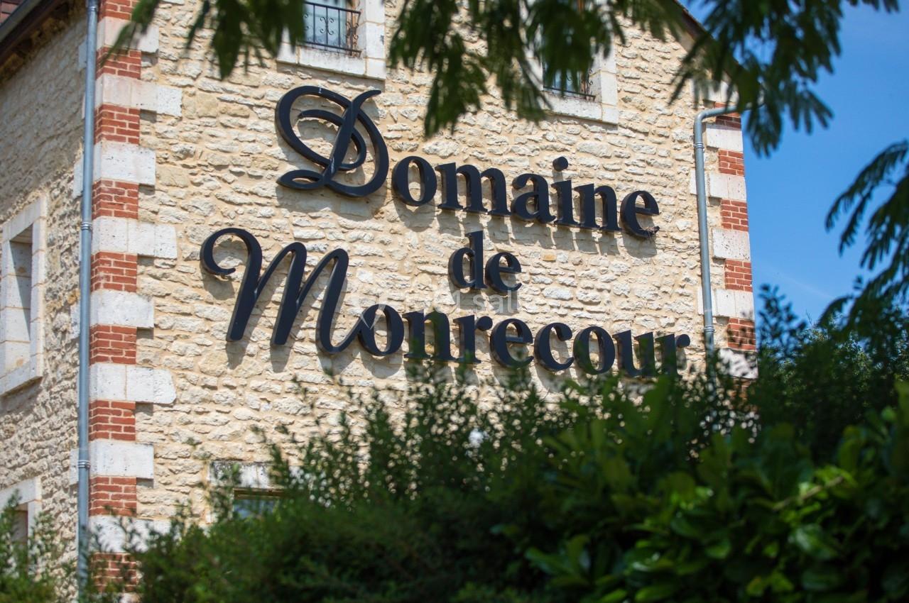Façade en pierre avec l'inscription ’Domaine de Monrecour’ en lettres noires, entourée de verdure.