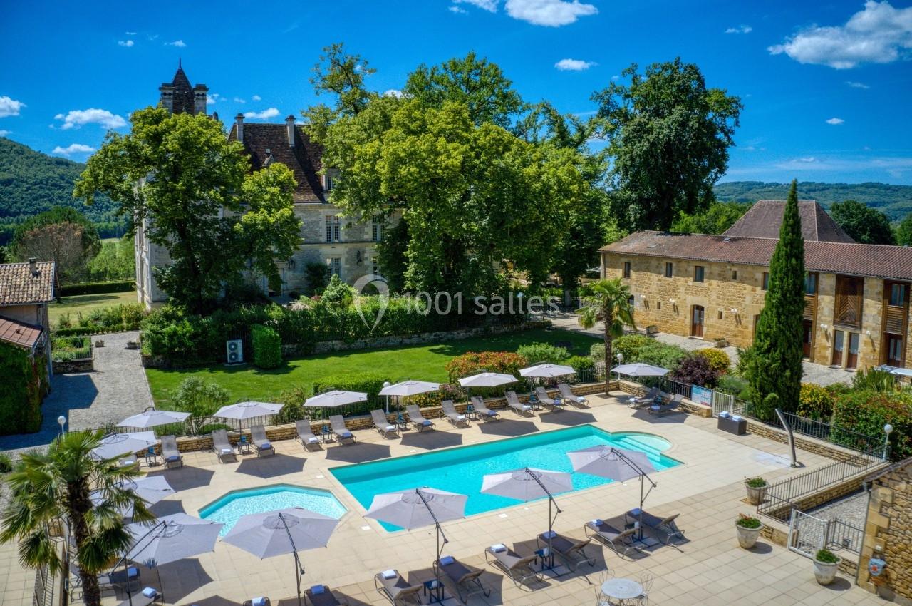 Piscine extérieure entourée de chaises longues et parasols, avec un château et des arbres en arrière-plan.