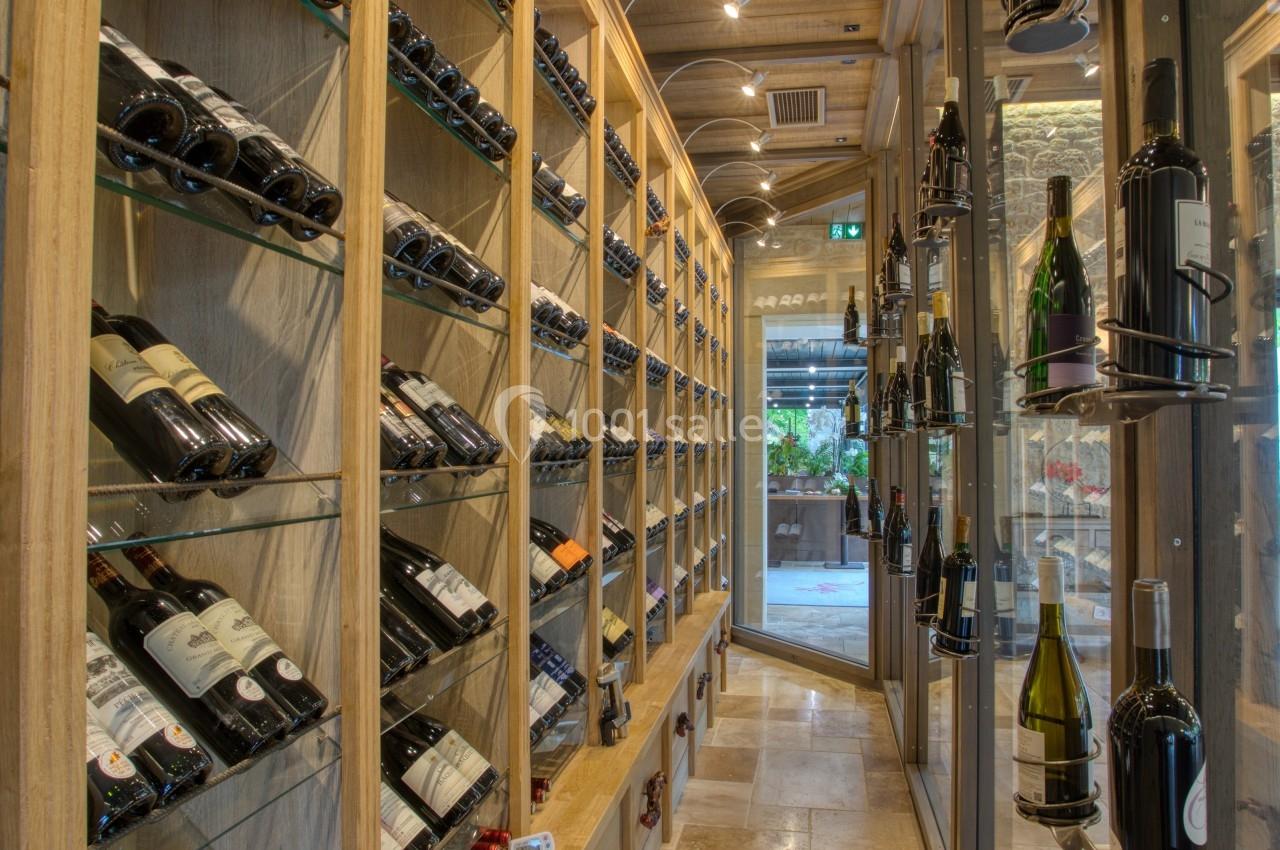 Cave à vin avec étagères en bois remplies de bouteilles, éclairage tamisé et sol en pierre beige.