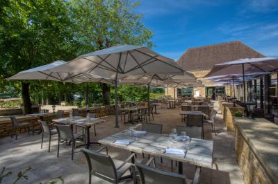Table en bois dressée avec des verres, des couverts et des serviettes blanches, en extérieur avec un fond de verdure.