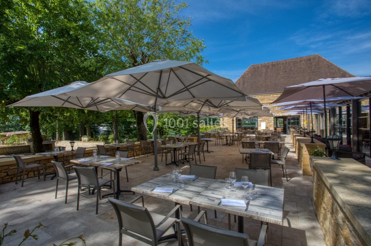 Terrasse d'un restaurant avec tables dressées, chaises et grands parasols, entourée de verdure et baignée de lumière…