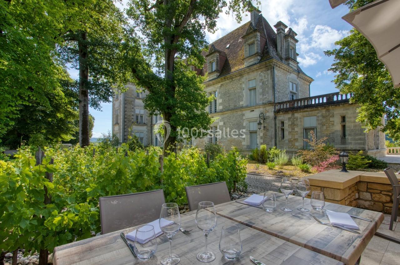 Table dressée en extérieur avec vue sur un château en pierre entouré de verdure et de vignes.
