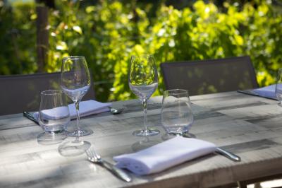 Table en bois dressée avec des verres, des couverts et des serviettes blanches, en extérieur avec un fond de verdure.
