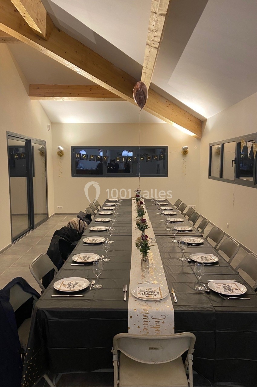 Table décorée pour un anniversaire dans une salle moderne, avec nappes noires, guirlandes et ballons suspendus.