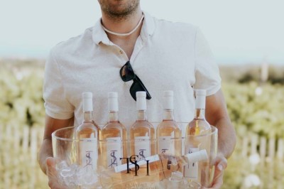 Miniature Location salle La Londe-les-Maures (Var) - Château Tour Saint Honoré #14 Un homme tenant un seau transparent rempli de bouteilles de vin rosé, en extérieur avec un fond flou de verdure.