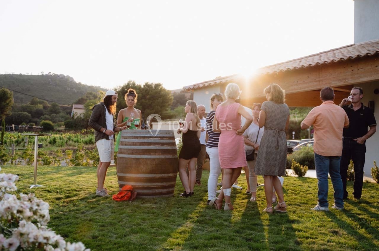 Groupe de personnes discutant autour d'un tonneau transformé en table dans un jardin au coucher du soleil.