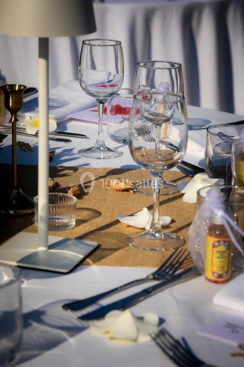 Table dressée avec nappe blanche, verres à pied, couverts, décorations marines et pétales de fleurs.