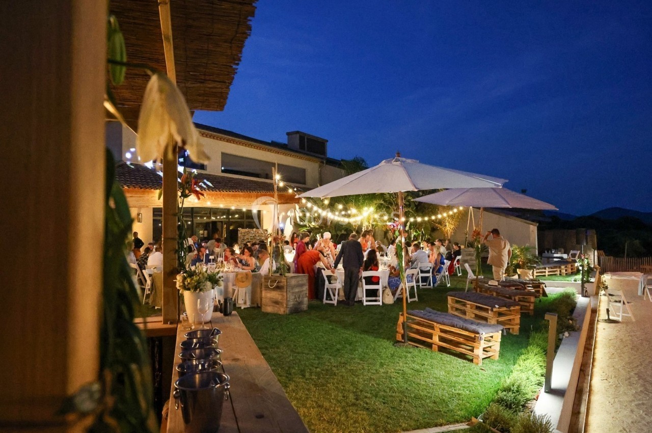Dîner en plein air sous des guirlandes lumineuses dans un jardin, avec des invités assis autour de tables décorées.
