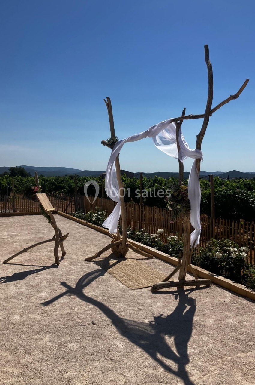 Structure en bois décorée de voiles blancs, installée en extérieur devant des vignes sous un ciel dégagé.