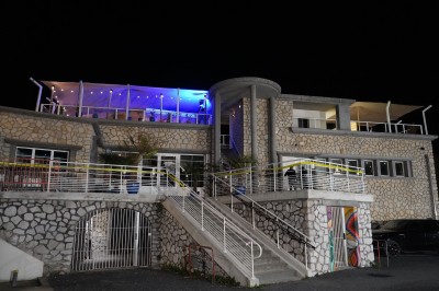 Bar moderne avec éclairage bleu, étagères remplies de bouteilles et ambiance tamisée.