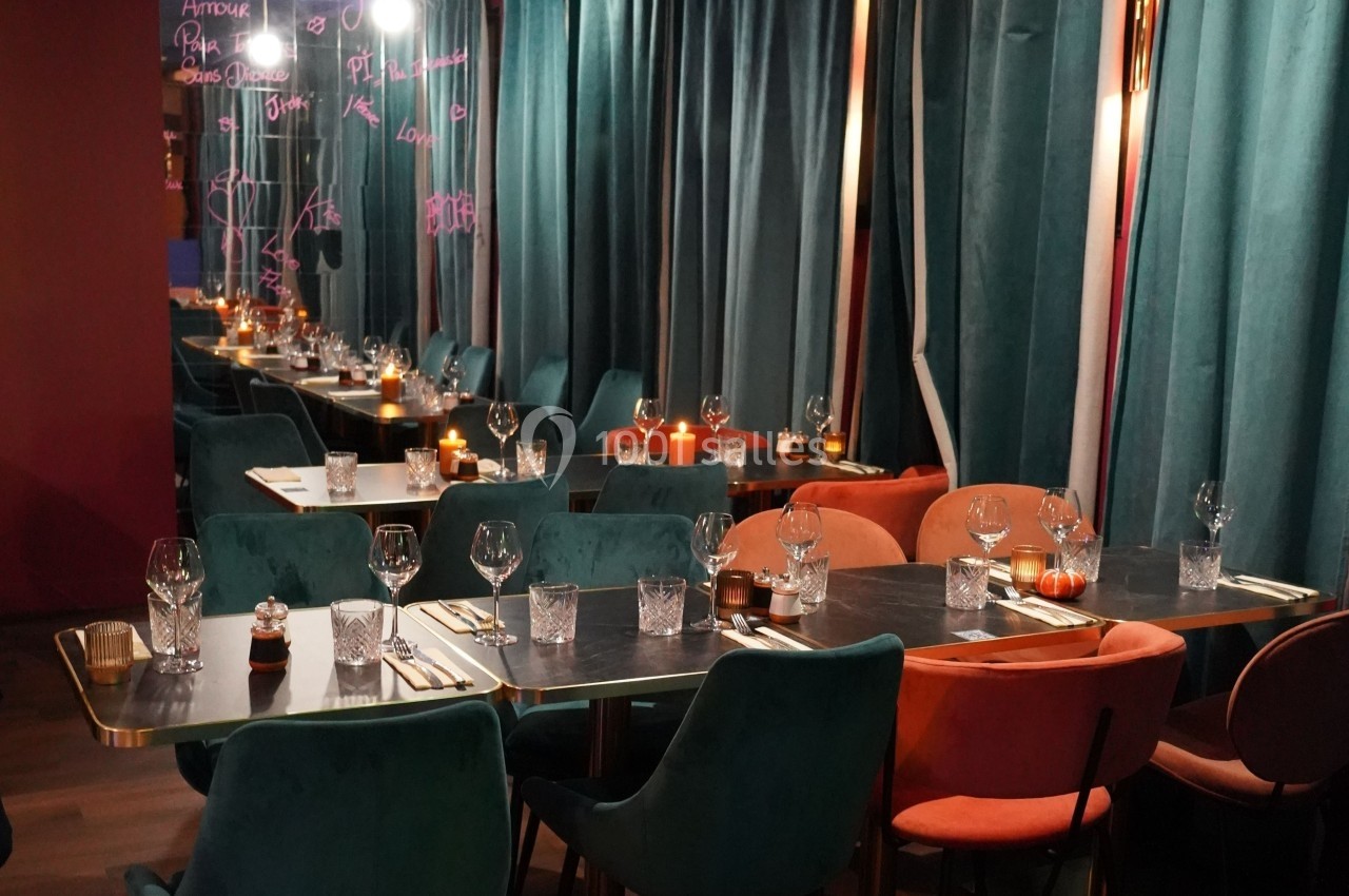 Salle de restaurant élégante avec tables dressées, chaises colorées et rideaux en velours vert.