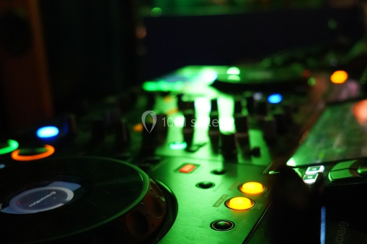 Console de mixage DJ éclairée avec des boutons colorés et des platines dans une ambiance sombre.