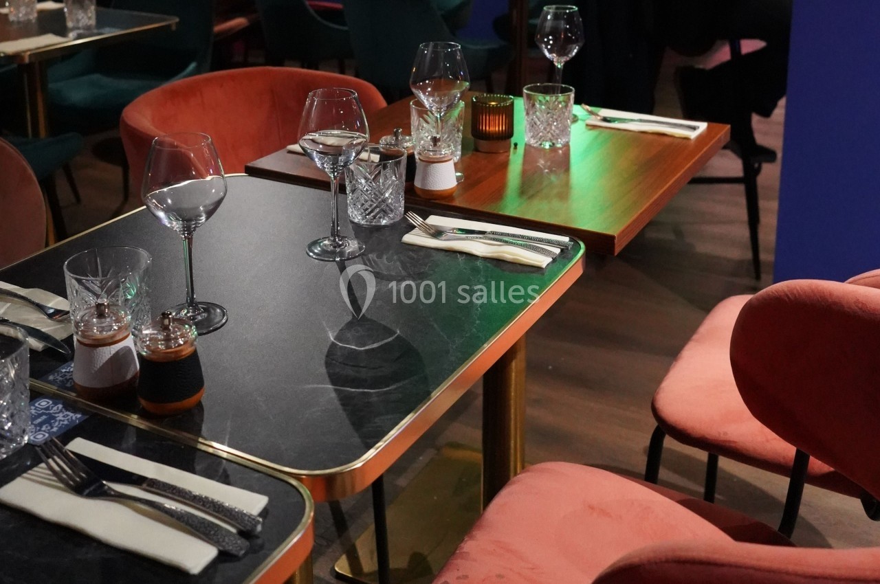 Tables de restaurant élégamment dressées avec verres, couverts et serviettes, entourées de chaises en velours rose.