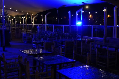 Bar moderne avec éclairage bleu, étagères remplies de bouteilles et ambiance tamisée.