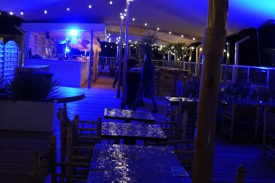 Bar moderne avec éclairage bleu, étagères remplies de bouteilles et ambiance tamisée.