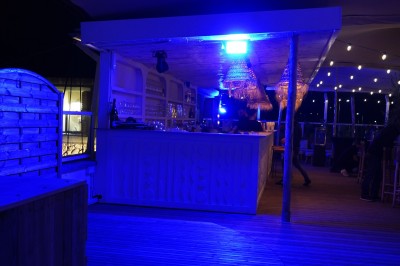 Bar moderne avec éclairage bleu, étagères remplies de bouteilles et ambiance tamisée.