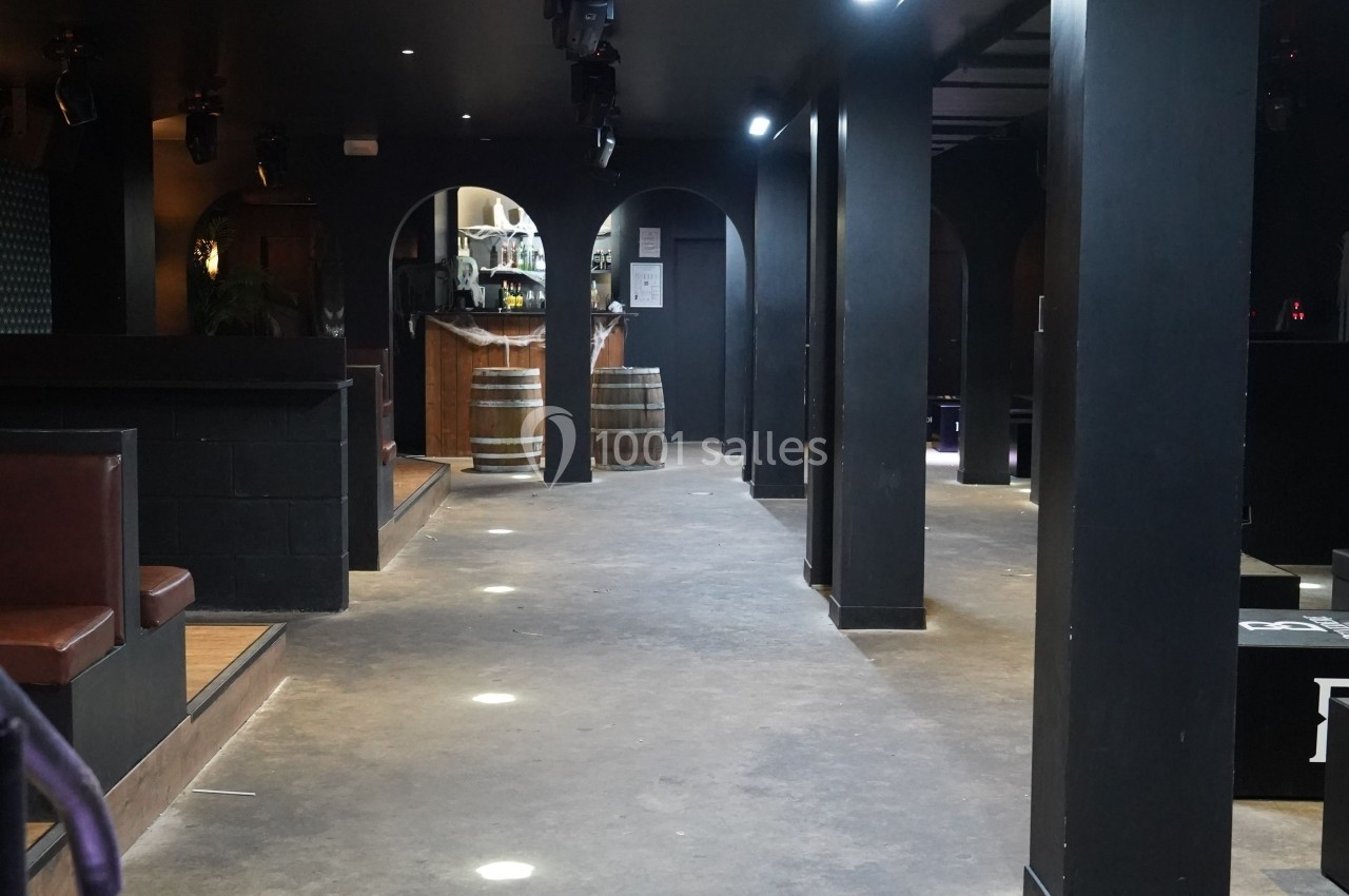 Salle intérieure sombre avec piliers noirs, banquettes en cuir marron et tonneaux en bois près d'un comptoir.