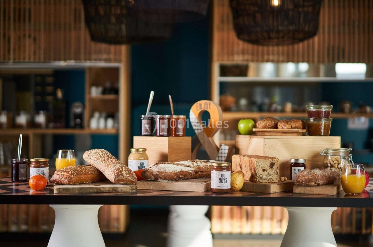 Buffet de petit-déjeuner avec pains, confitures, jus de fruits et viennoiseries disposés sur une table en bois.
