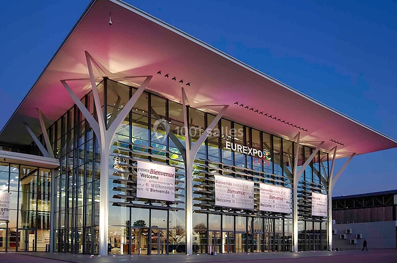 Façade moderne et vitrée du bâtiment Eurexpo éclairée à la tombée de la nuit.